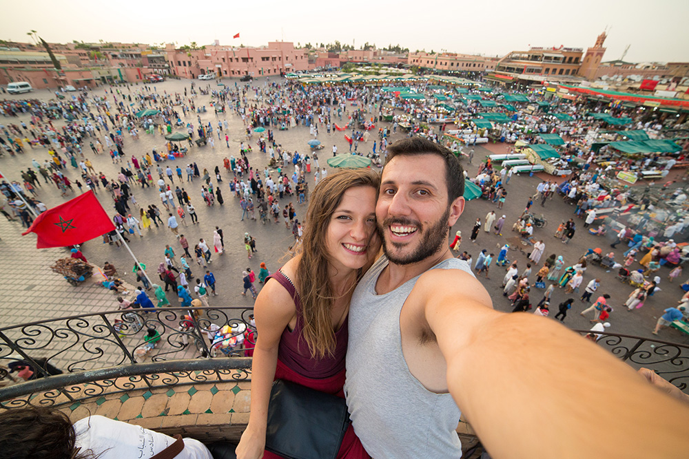 Una pareja haciendose un selfie y de fondo la plaza llena de gente paseando entre sus puestos