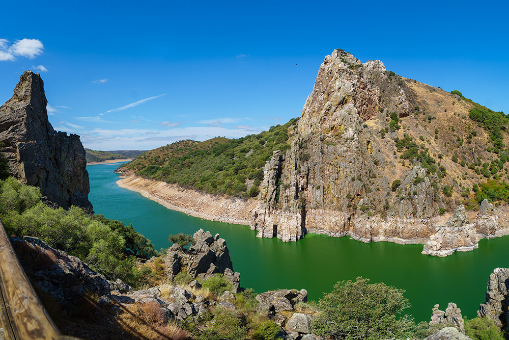 Rio de agua verde entre pequeñas montañas marrones y verdes. Un cielo azul nítido de fondo 
