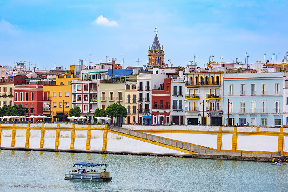 Orilla del rio Guadalquivir correspondiente al barrio sevillano de Triana. Casas de diversos colores y en el rio surcando un barco