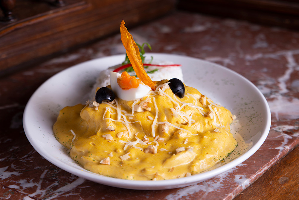 Guiso cremoso de color amarillo coronado por dos olivas negras y un huevo duro. Al costado de acompañamiento arroz blanco con perejil decorando