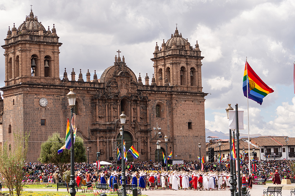 Una iglesia bajo un cielo gris. Frente a ella una multitud de gente con túnicas y varias banderas izadas .