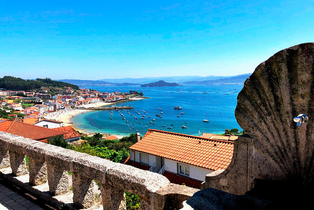 Vistas desde un balcón de piedra de una bahía con playa y casas alrededor