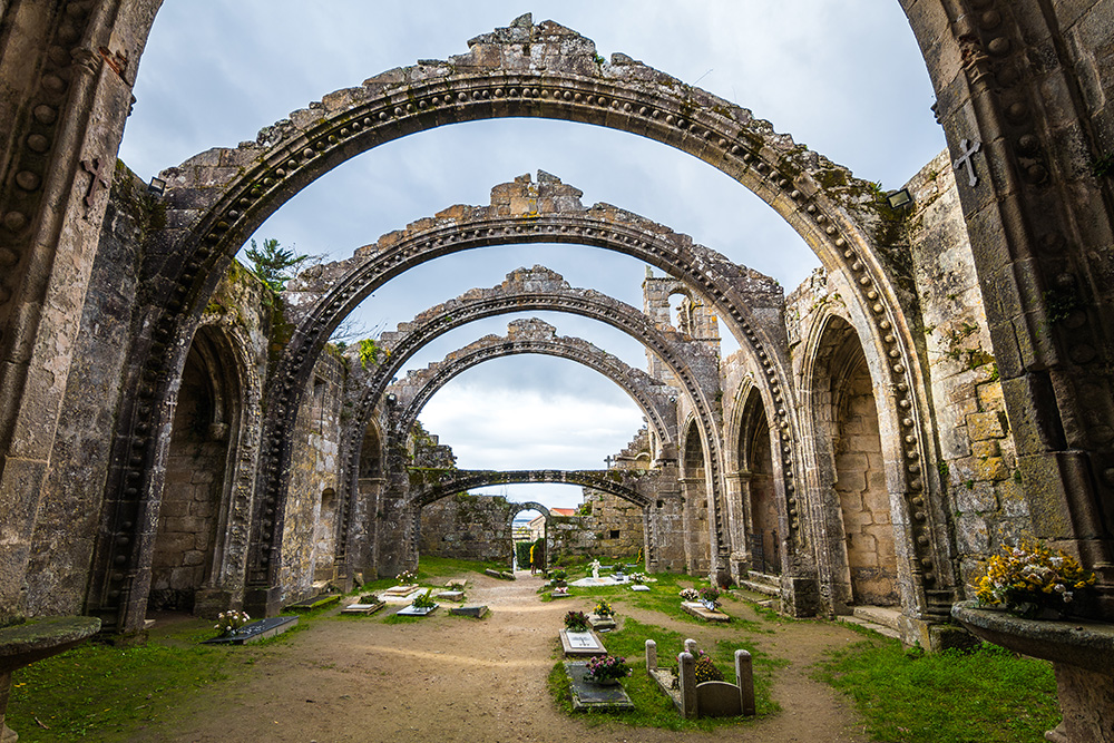 Un estructura en arcos, similar a una iglesia sin tejado. El interior es camino de tierra con vegetación y pequeñas tumbas con lapidas