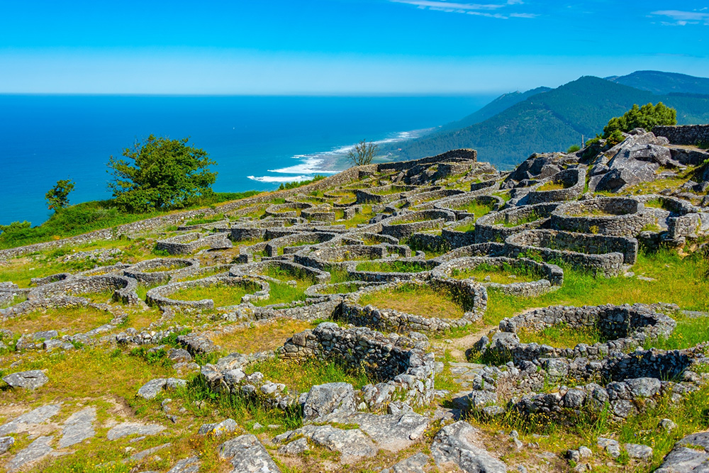 Pequeño monte con vistas al mar azul. El monte cubierto de círculos de piedra y verde