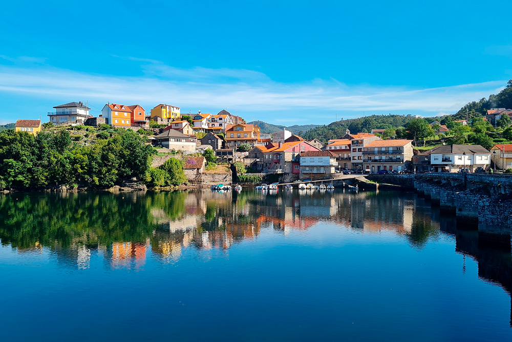 Una bahia y en tierra un pequeño pueblo rodeado de verde y un cielo azul