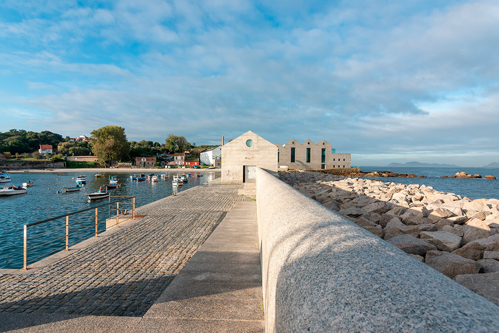 Museo al fondo de un camino de piedra y rodeado de mar bajo un cielo azul con nubes