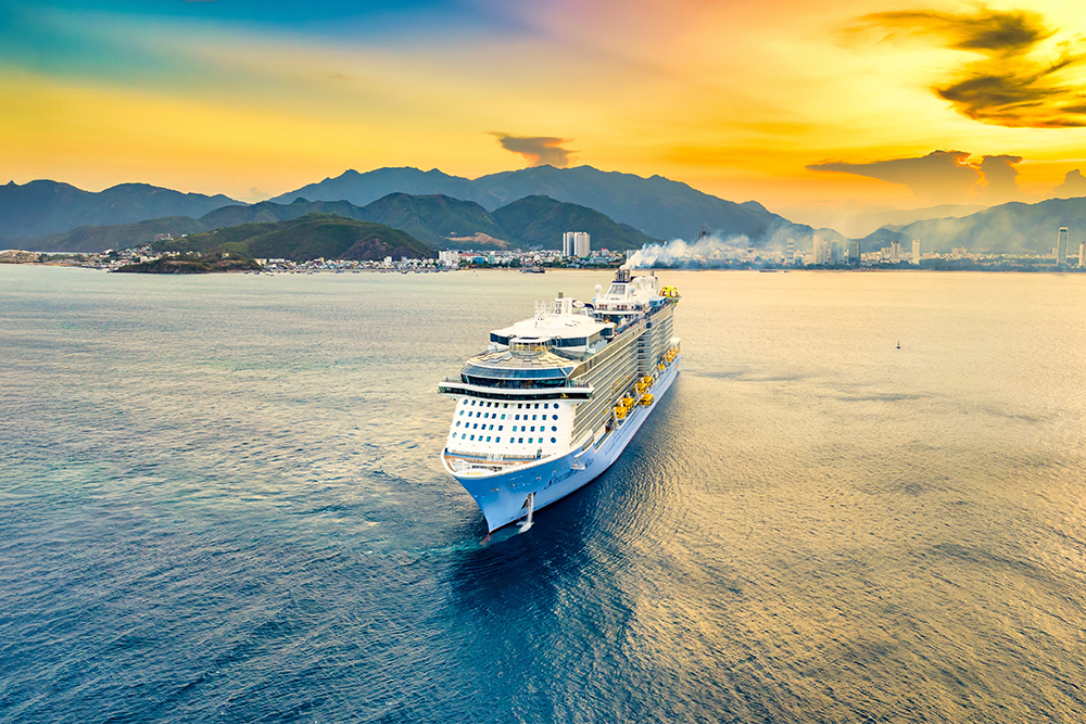 Crucero en medio del mar con el puerto de fondo. Montañas bajo un atardecer en tonos amarillos