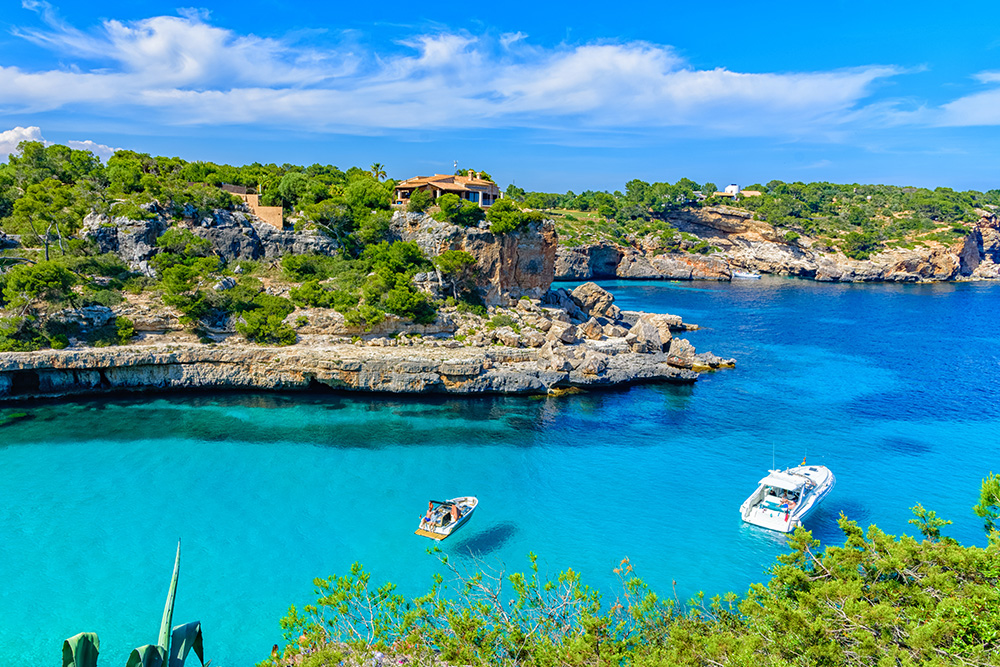 Una bahía con dos barquitos en un mar azul turquesa y de fondo una casa rodeada de arboles