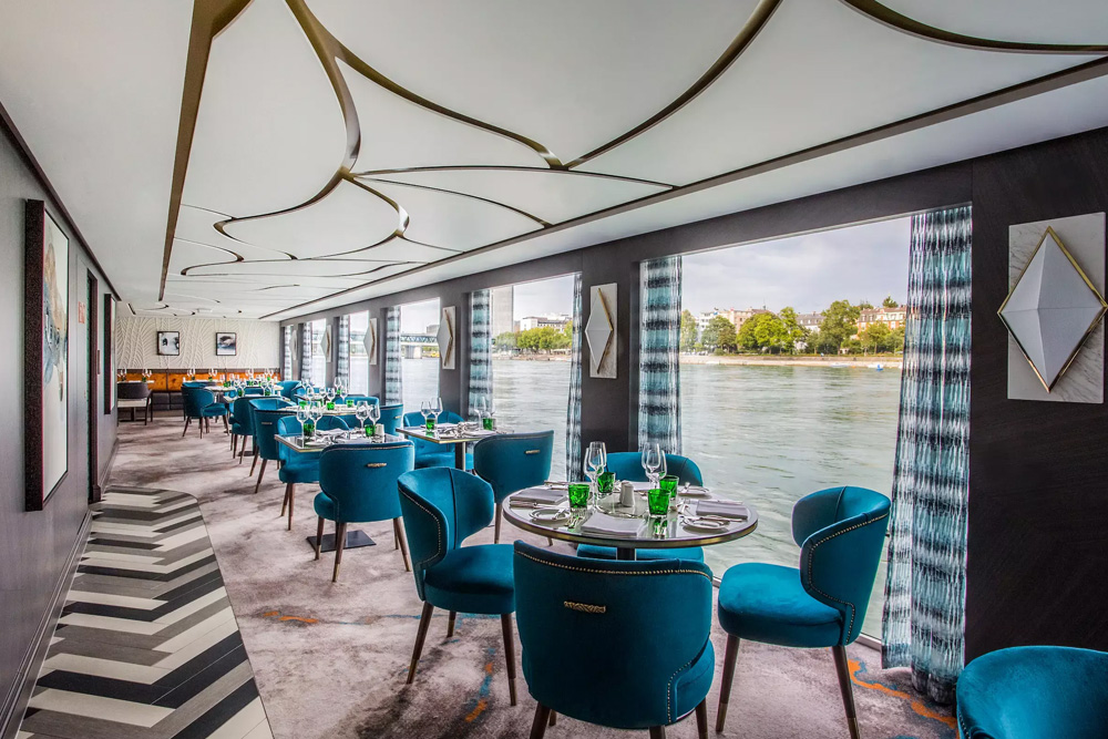 Mesas redondas con el servicio puesto. Sillones en tono aguamarina y varias ventanales con vista al mar